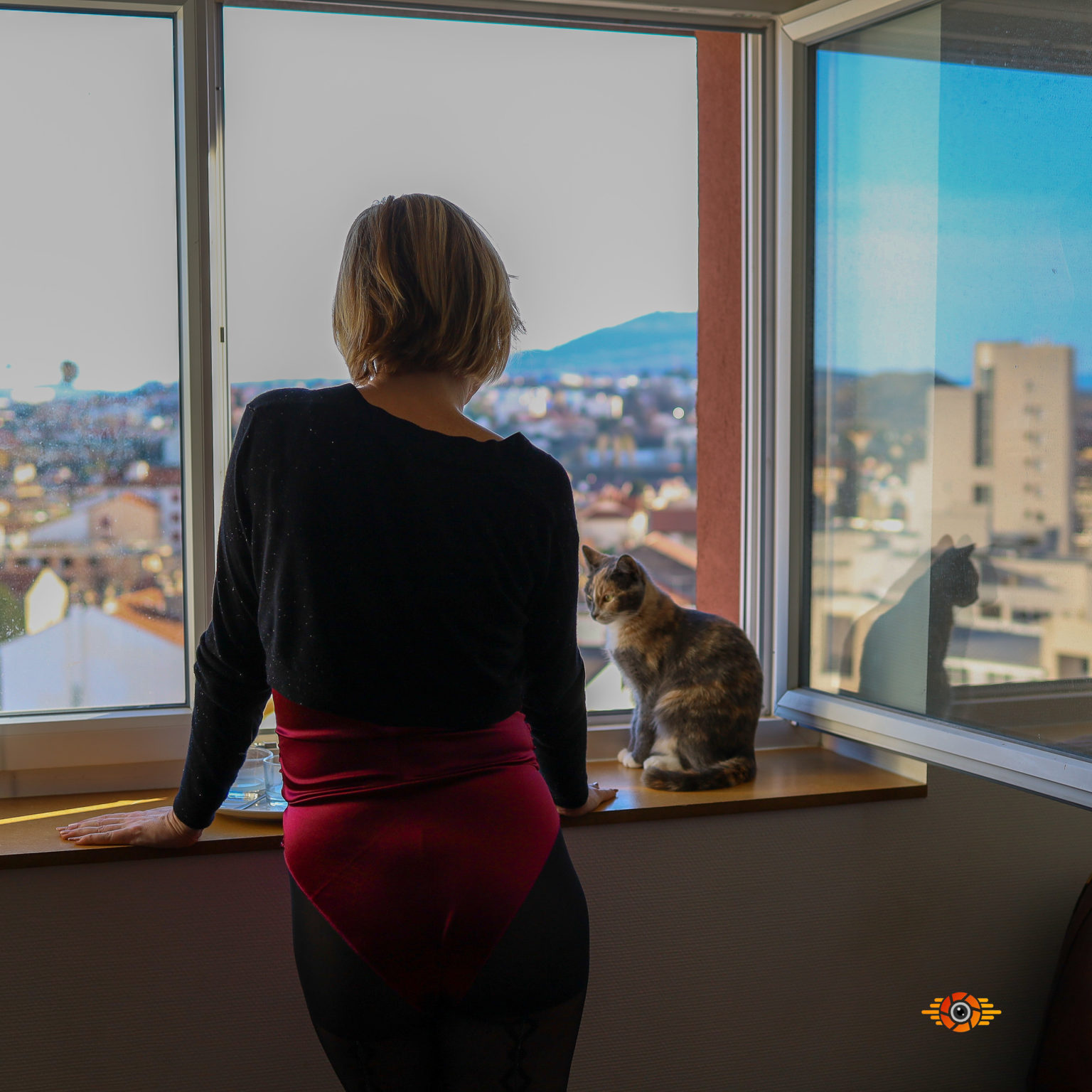 une femme est à la fenêtre avec un chat à ses cotés